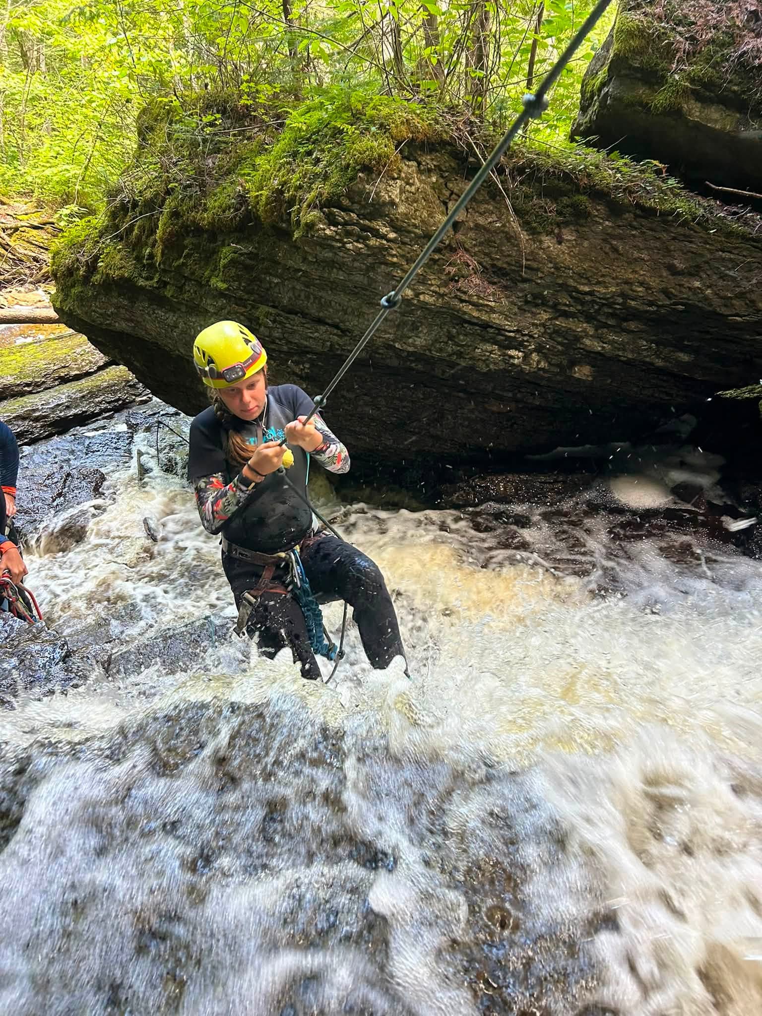 un homme au casque jaune fait du rappel dans un ruisseau