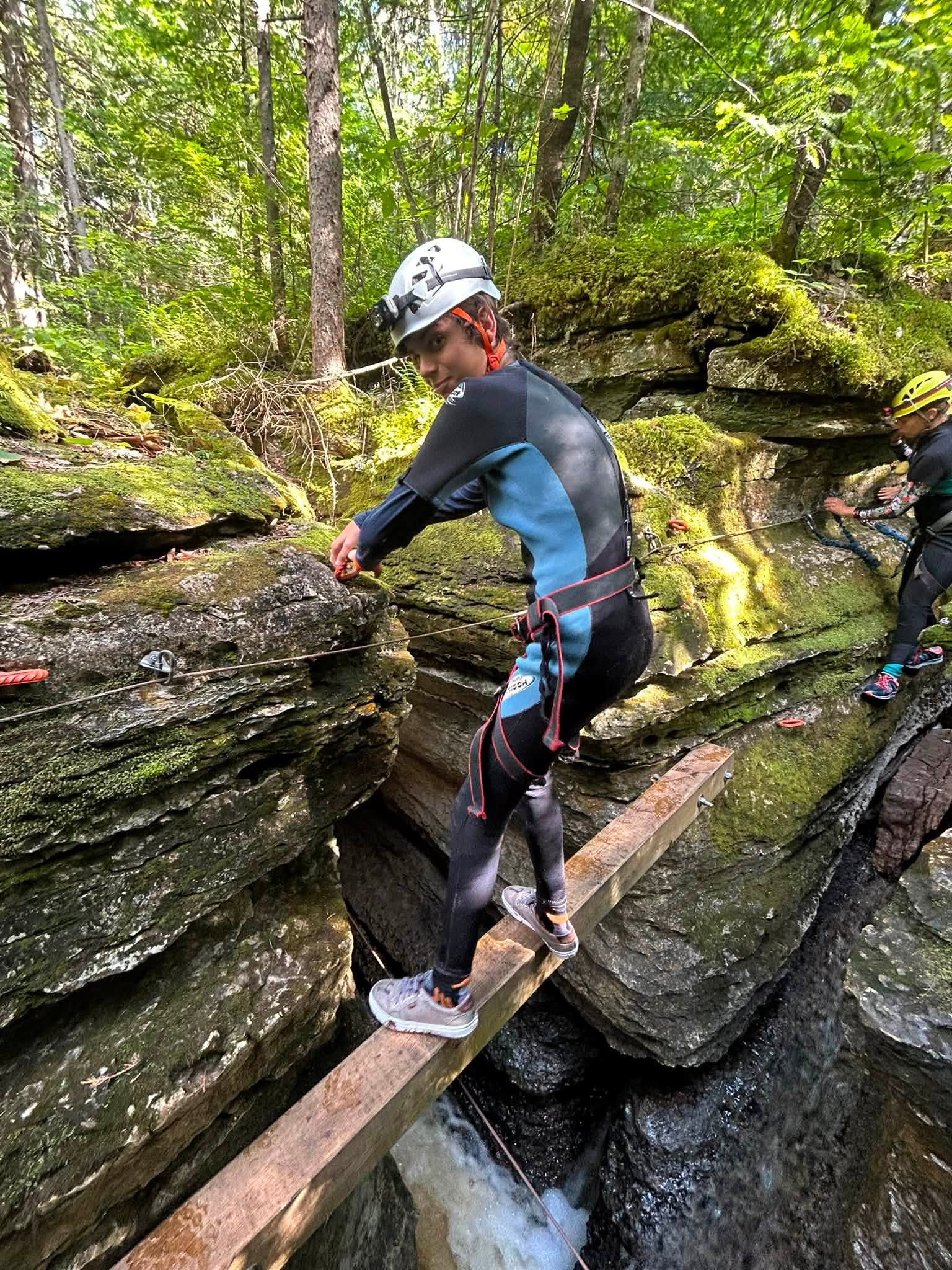 deux personnes en combinaison et casque traversent un petit ruisseau dans les bois