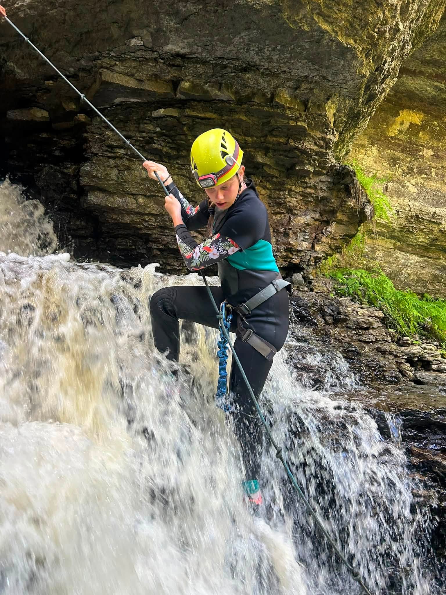 un homme au casque jaune descend en rappel une cascade