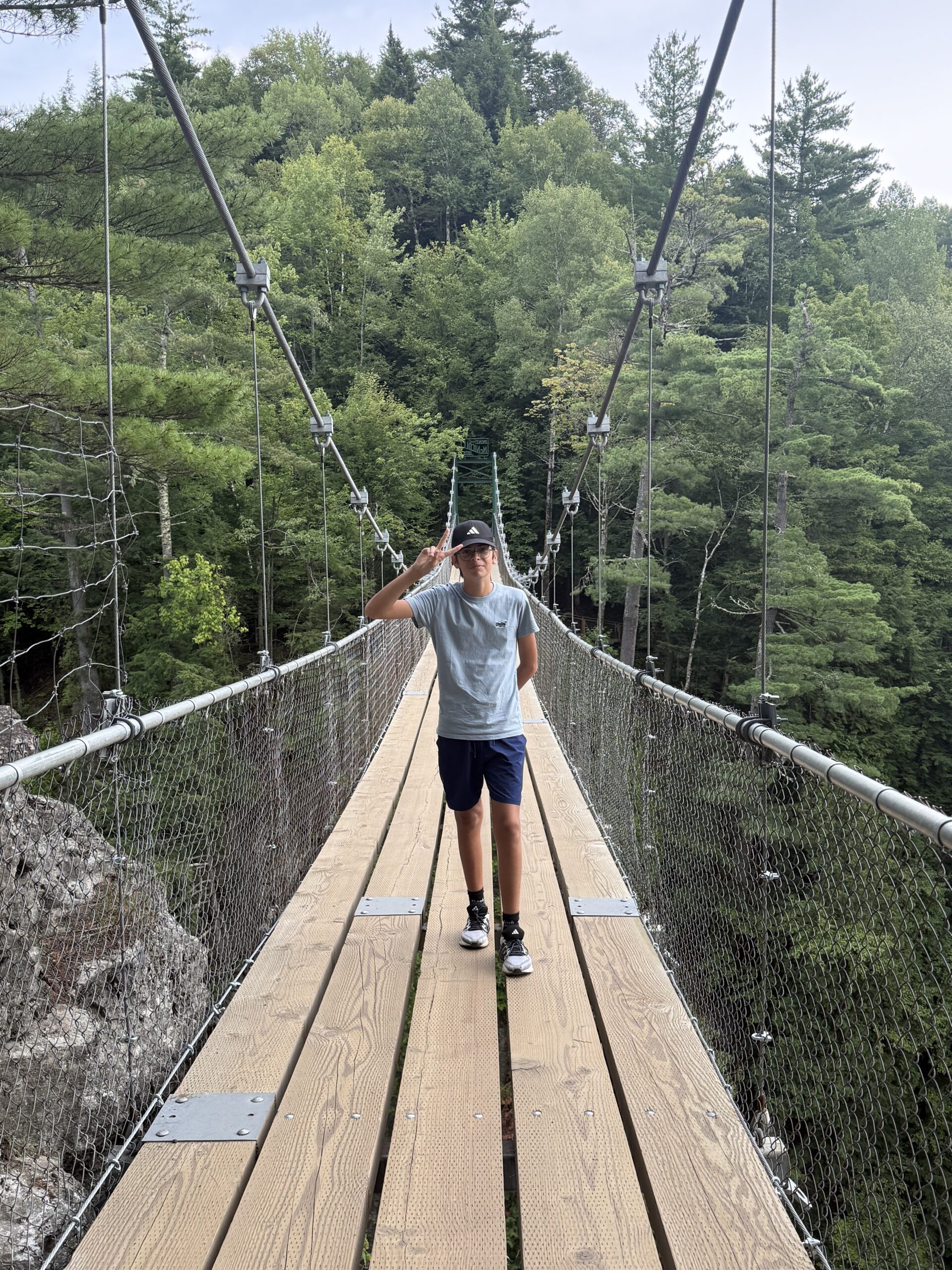 un homme traversant un pont en bois au-dessus d'une forêt, Saint-Ferréol-les-Neiges, Québec, Canada