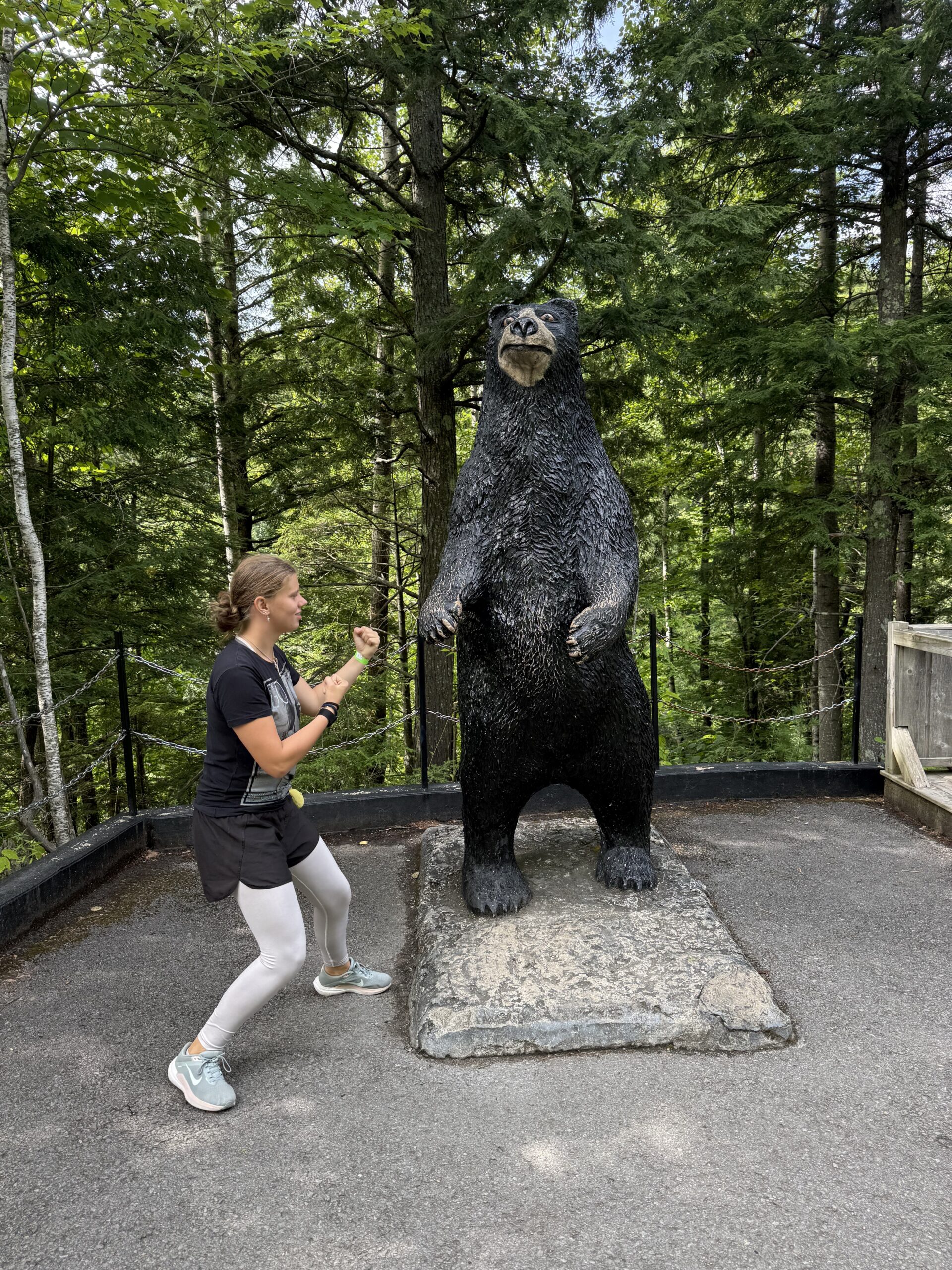 une femme accroupie sur un rocher à côté d'une grande statue d'ours, Saint-Joachim, Québec, Canada