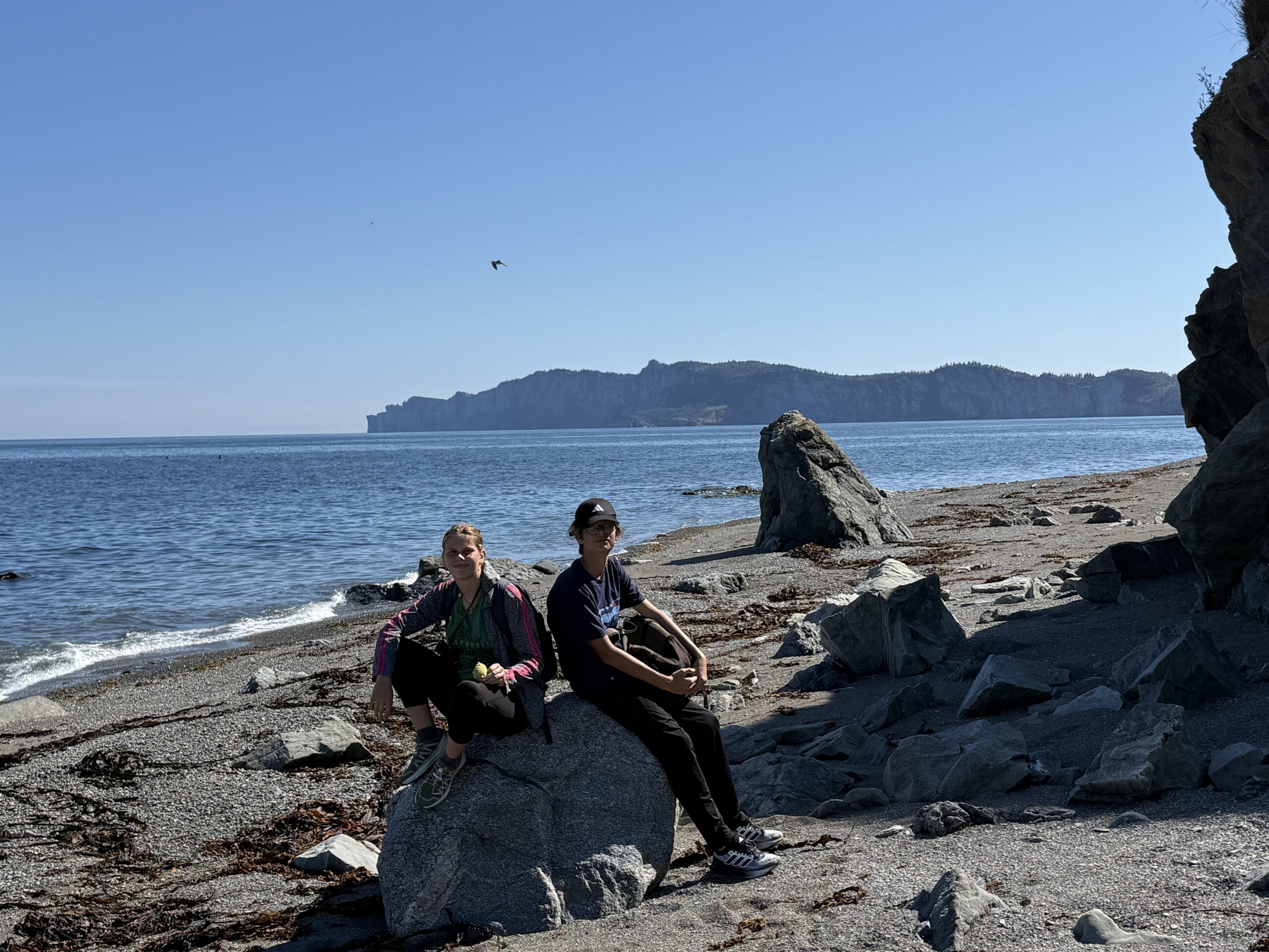 two people sitting on rocks near the water, Gaspé, Québec, Canada