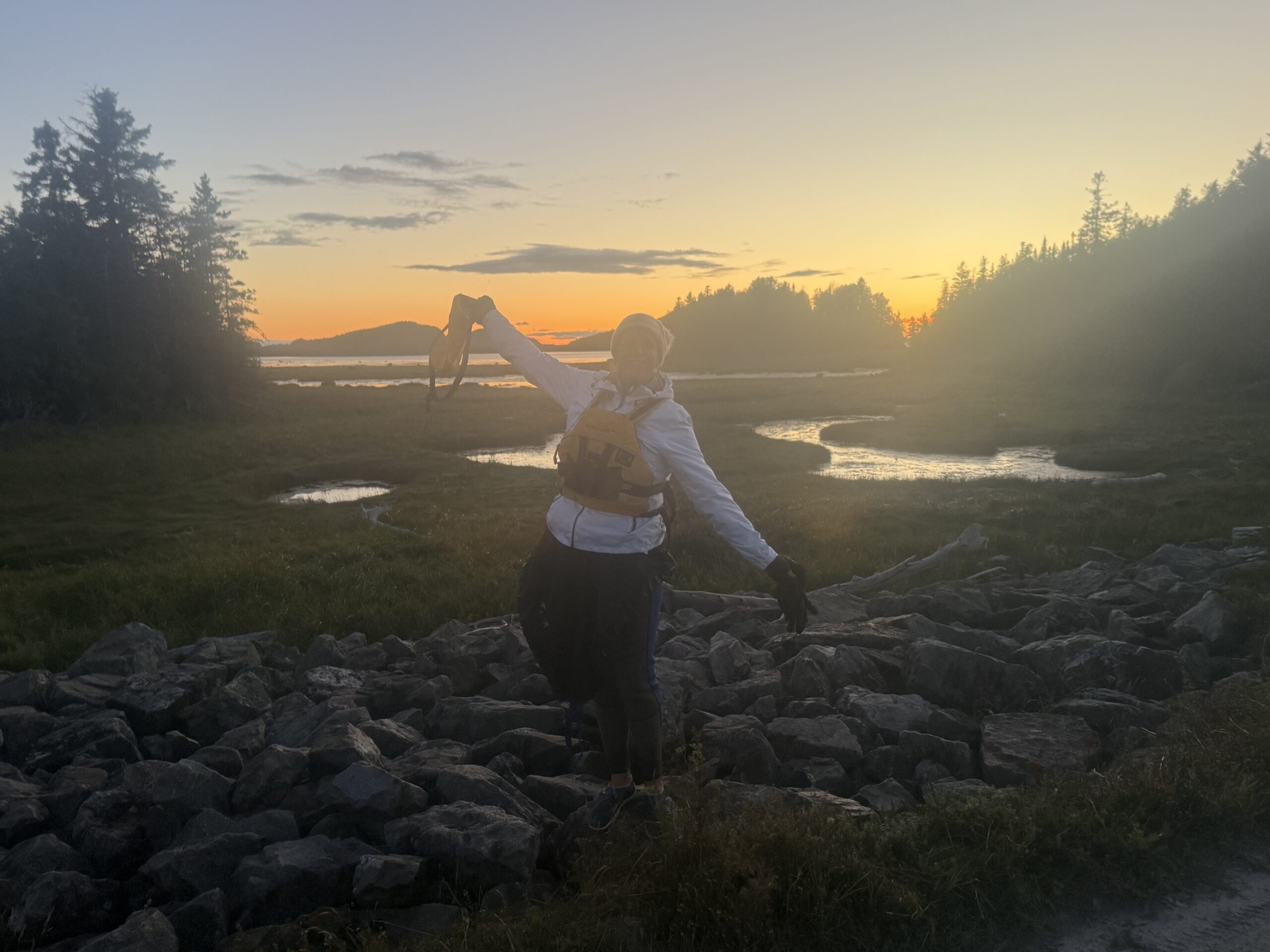 a man standing on a rocky shore at sunset, Rimouski, Québec, Canada